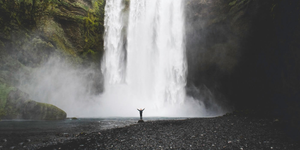 A huge waterfall in the background and a small figure standing at the bottom, raising their arms.
